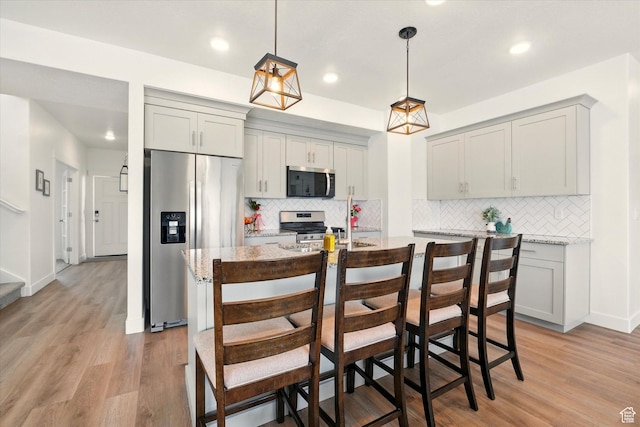 1412 W 1920 S, Logan, UT 84321 - kitchen with appliances with stainless steel finishes, gray cabinetry, tasteful backsplash, light wood finished floors, and a kitchen bar