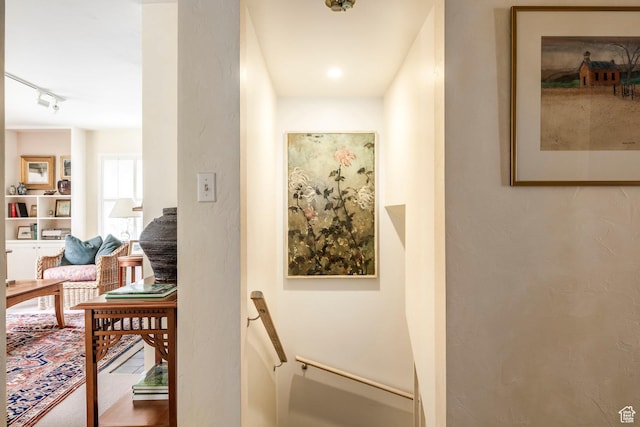 corridor featuring rail lighting and an upstairs landing