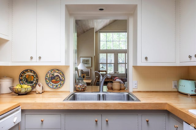 kitchen featuring a sink, lofted ceiling, tasteful backsplash, dishwashing machine, and white cabinets