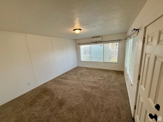 empty room featuring an AC wall unit, carpet flooring, and a textured ceiling