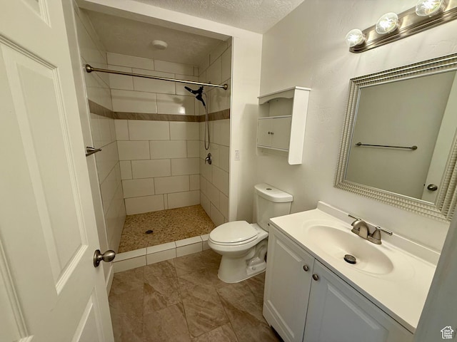bathroom with toilet, vanity, a tile shower, and a textured ceiling