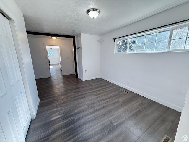 empty room with a textured ceiling, dark wood-type flooring, baseboards, and healthy amount of natural light