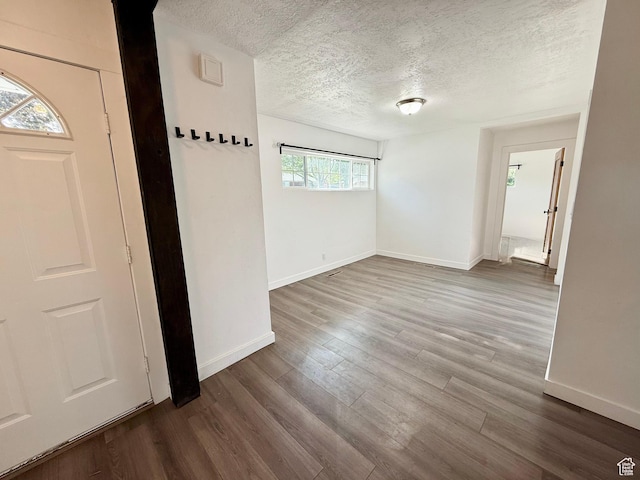 empty room featuring a textured ceiling, baseboards, and dark wood finished floors