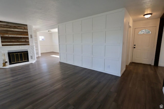 unfurnished living room with a glass covered fireplace, dark wood-style flooring, a decorative wall, and a textured ceiling