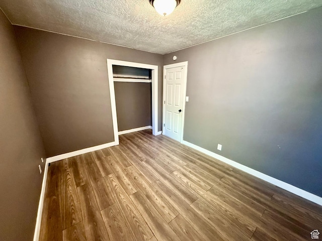 unfurnished bedroom with wood finished floors, baseboards, a closet, and a textured ceiling