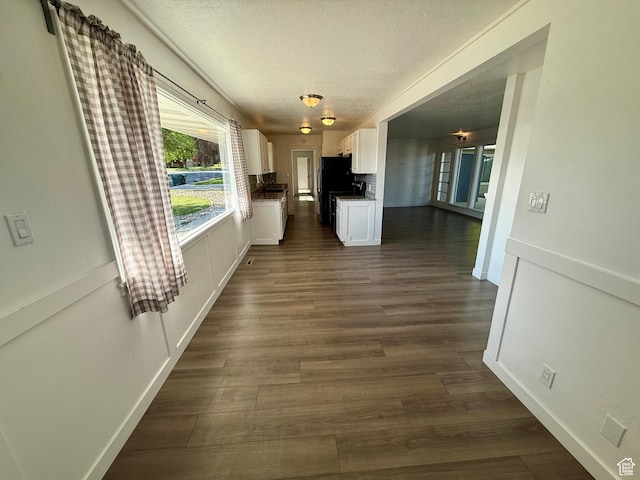 hall featuring a textured ceiling, dark wood finished floors, and baseboards
