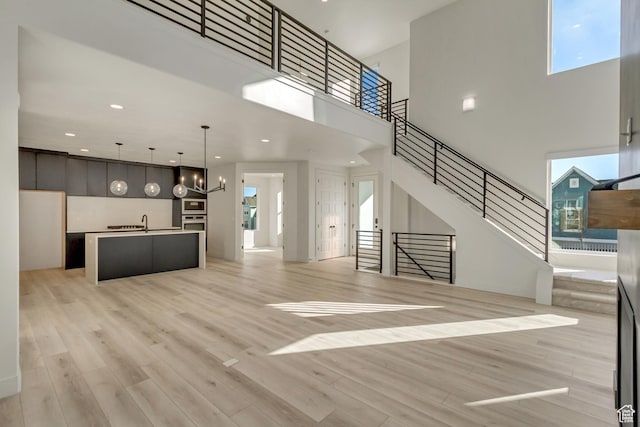 6904 W Lake Ave S Unit 213, South Jordan, UT 84009 - unfurnished living room featuring a towering ceiling, light wood finished floors, a chandelier, stairway, and recessed lighting