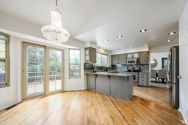 kitchen featuring appliances with stainless steel finishes, gray cabinets, a peninsula, a chandelier, and light wood-style floors