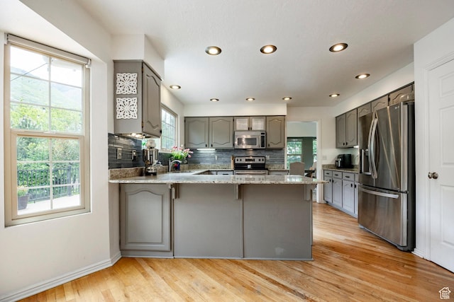 kitchen with appliances with stainless steel finishes, gray cabinets, a peninsula, tasteful backsplash, and light wood finished floors