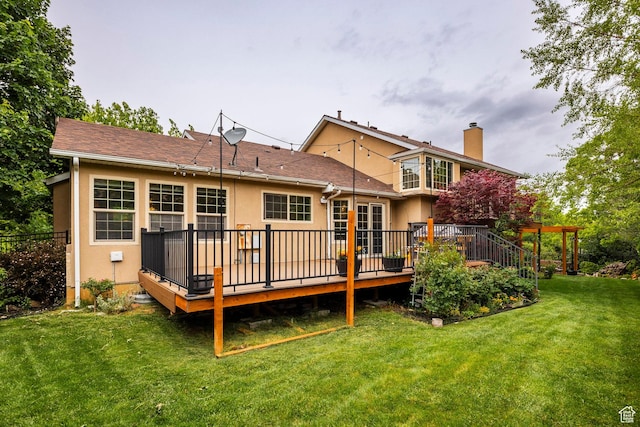 rear view of house featuring a chimney, stucco siding, a wooden deck, and a yard