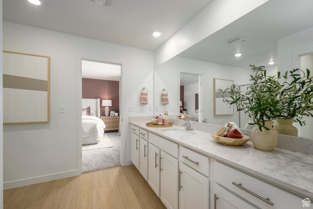 ensuite bathroom featuring wood finished floors, vanity, and recessed lighting