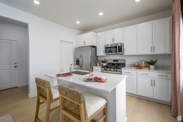 kitchen featuring stainless steel appliances, a kitchen island with sink, white cabinetry, light wood-style floors, and recessed lighting