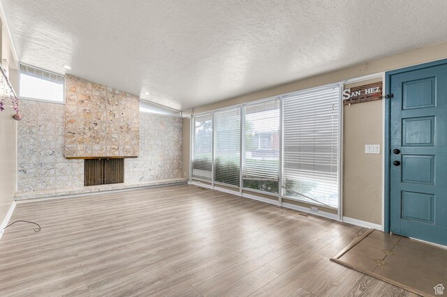 2011 W Todd Way S, Taylorsville, UT 84129 - unfurnished living room featuring a textured ceiling, wood finished floors, healthy amount of natural light, a stone fireplace, and baseboards