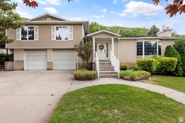 573 S Cherry Ln, Fruit Heights, UT 84037 - split level home with an attached garage, concrete driveway, a front lawn, a chimney, and brick siding