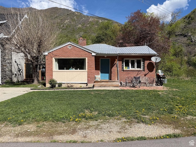 single story home with a front yard, a chimney, brick siding, metal roof, and a mountain view