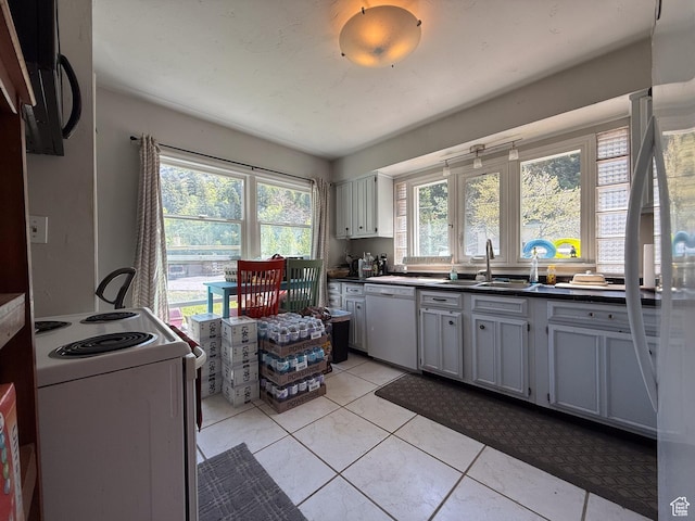 kitchen featuring white appliances, a sink, dark countertops, and plenty of natural light