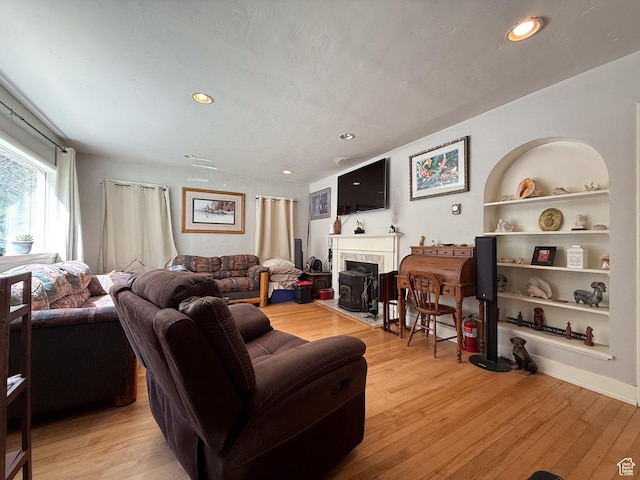 living room with light wood-style flooring, built in features, a premium fireplace, and recessed lighting