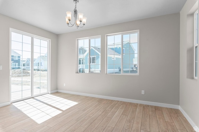 empty room with a chandelier, light wood-style flooring, baseboards, and healthy amount of natural light