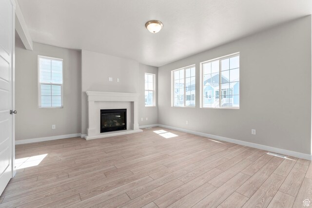 unfurnished living room with light wood-type flooring, baseboards, and a glass covered fireplace