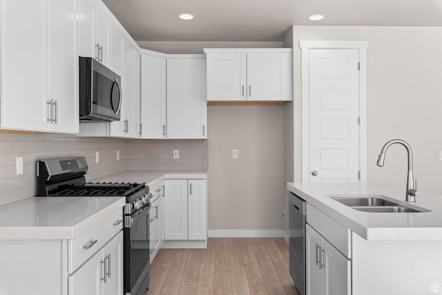 kitchen with appliances with stainless steel finishes, a sink, light wood-type flooring, recessed lighting, and white cabinets