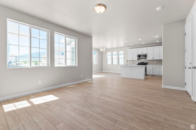 unfurnished living room with a chandelier, baseboards, light wood finished floors, recessed lighting, and a sink