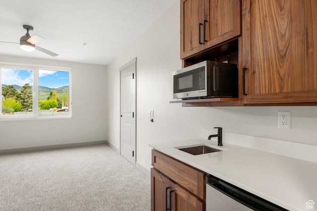 kitchen featuring stainless steel microwave, a sink, brown cabinets, light carpet, and a ceiling fan