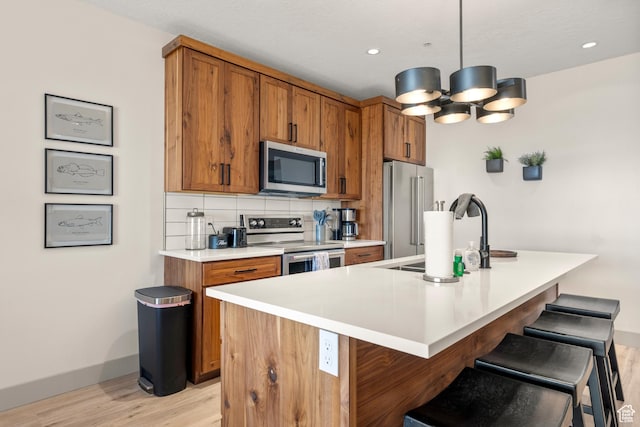 kitchen featuring appliances with stainless steel finishes, brown cabinets, light wood-style flooring, a sink, and a breakfast bar