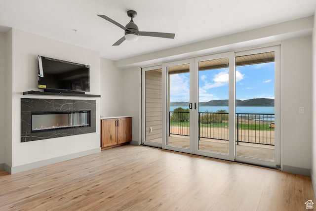 unfurnished living room featuring light wood-style flooring, a premium fireplace, ceiling fan, and baseboards