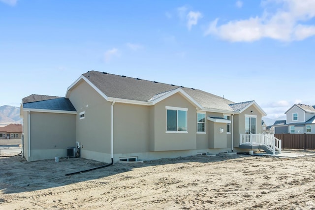 view of front facade with cooling unit, stucco siding, and roof with shingles