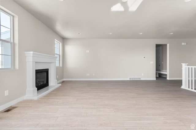 unfurnished living room featuring light wood finished floors, a glass covered fireplace, baseboards, and recessed lighting
