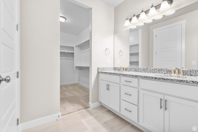 full bath featuring baseboards, double vanity, and a spacious closet