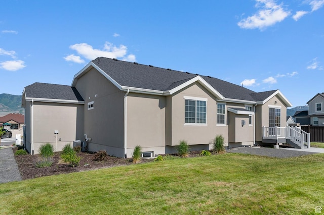 5667 N Parkview Dr, Stansbury Park, UT 84074 - back of property with a deck, a yard, stucco siding, central AC unit, and roof with shingles
