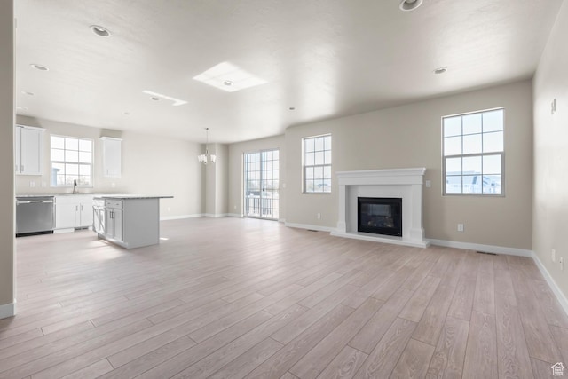 unfurnished living room with a chandelier, baseboards, light wood-style flooring, and a glass covered fireplace