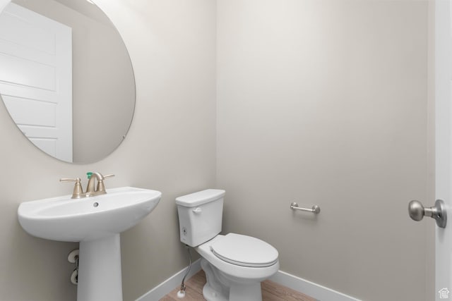 half bathroom with baseboards, toilet, wood finished floors, and a sink