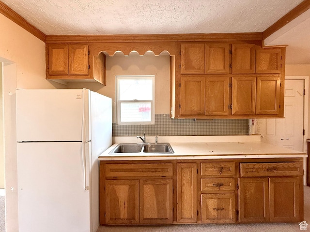 kitchen featuring freestanding refrigerator, a sink, brown cabinets, a textured ceiling, and light countertops