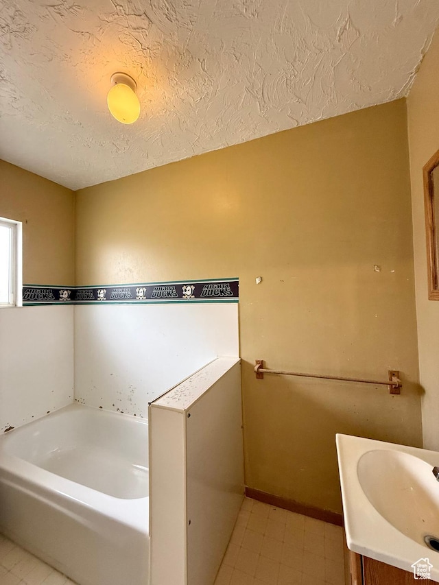 full bath featuring a garden tub, a textured ceiling, vanity, and baseboards