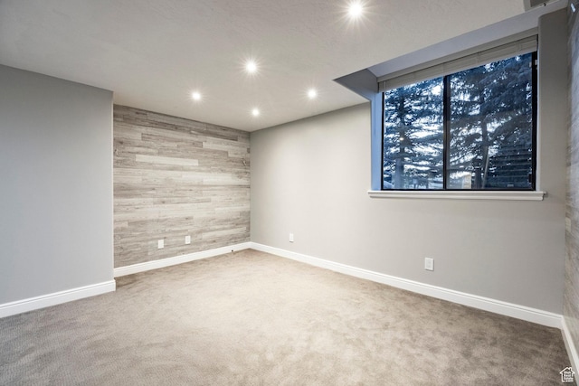 carpeted empty room featuring wooden walls, recessed lighting, baseboards, and an accent wall