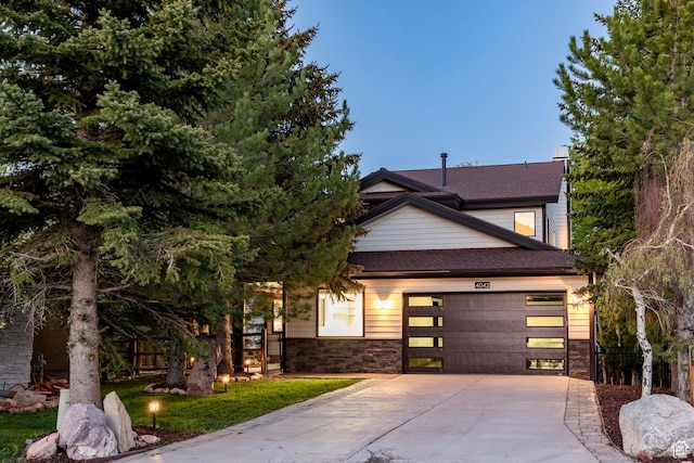 view of front of property featuring driveway, an attached garage, stone siding, and a shingled roof