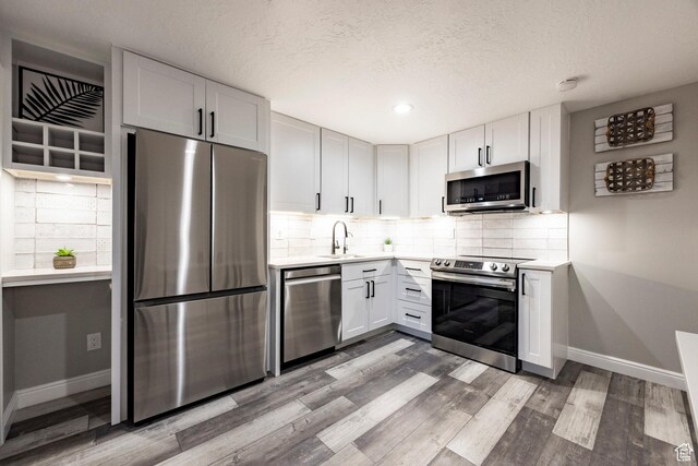 kitchen featuring appliances with stainless steel finishes, a sink, baseboards, light wood finished floors, and light countertops