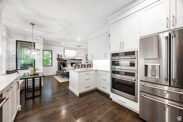 kitchen with appliances with stainless steel finishes, a peninsula, light countertops, white cabinetry, and dark wood finished floors