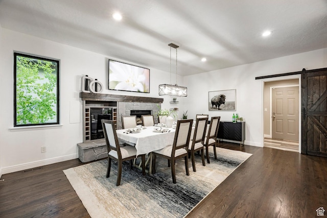 dining area featuring a barn door, a fireplace, baseboards, dark wood-type flooring, and recessed lighting