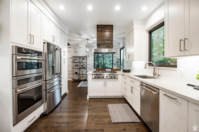 kitchen with appliances with stainless steel finishes, a peninsula, tasteful backsplash, white cabinets, and a sink