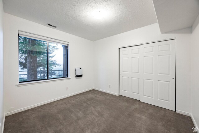 unfurnished bedroom featuring dark colored carpet, a textured ceiling, a closet, and baseboards