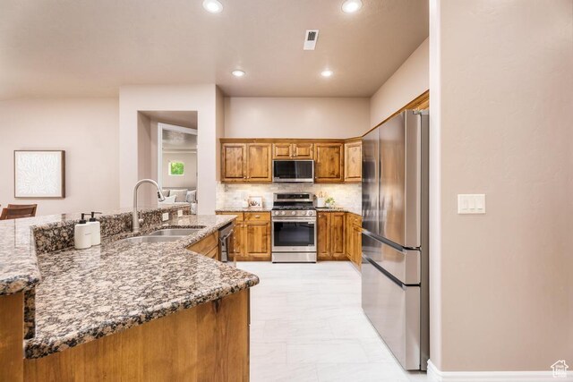 8 S Arroyo Dr, St George, UT 84790 - kitchen with stainless steel appliances, a sink, brown cabinetry, decorative backsplash, and light stone countertops