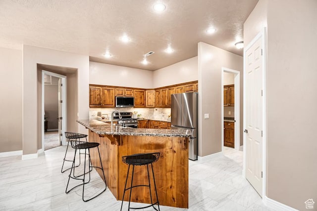 8 S Arroyo Dr, St George, UT 84790 - kitchen with stainless steel appliances, brown cabinetry, a kitchen breakfast bar, dark stone countertops, and a peninsula