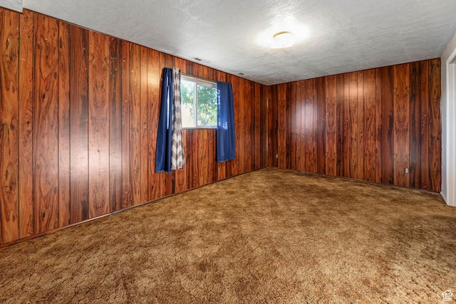 unfurnished room featuring a textured ceiling, carpet flooring, and wooden walls