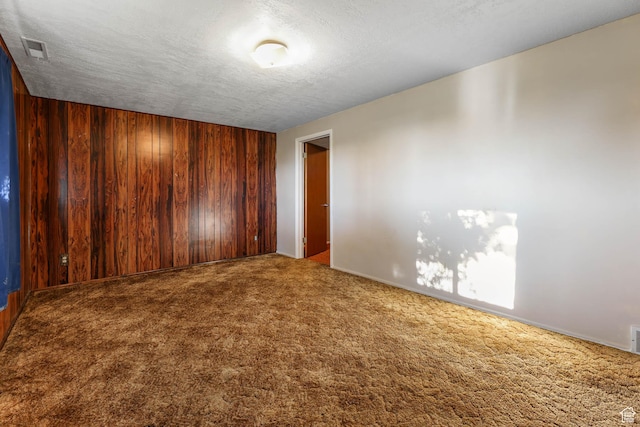 unfurnished room featuring carpet, a textured ceiling, wood walls, and baseboards