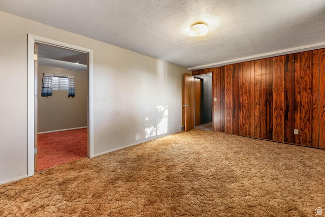 carpeted spare room with a textured ceiling, baseboards, and wood walls