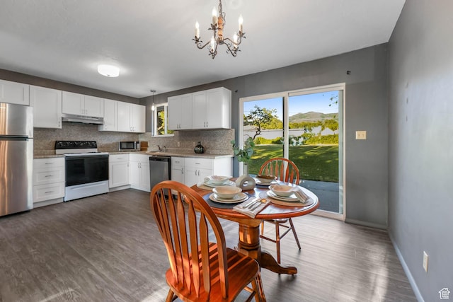 kitchen with appliances with stainless steel finishes, a chandelier, backsplash, white cabinetry, and under cabinet range hood