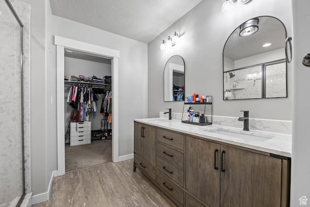 7886 N Bridleway Rd, Eagle Mountain, UT 84005 - bathroom featuring wood finished floors, a spacious closet, a shower stall, a textured ceiling, and double vanity
